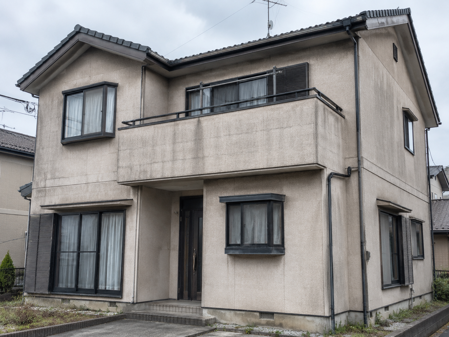 築20年ほどの2階建て戸建て住宅。外壁のベージュが色あせ、黒ずんだ汚れとひび割れが見える状態